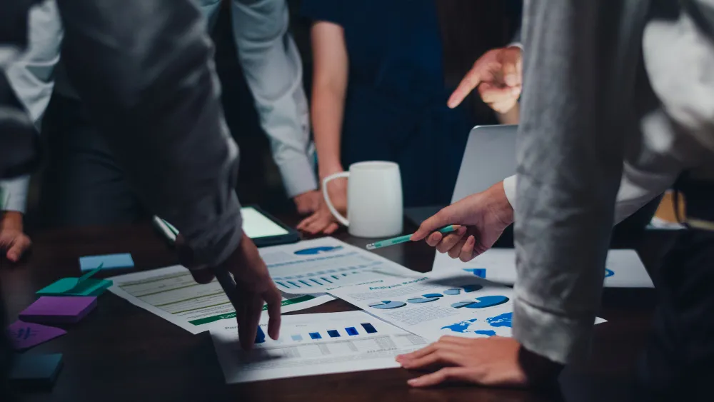 Hands of management team on the table pointing to the charts and other papers